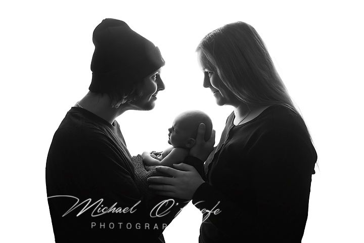 Black and white newborn photo of parents holding their baby, captured by Michael O'Keefe Photography.