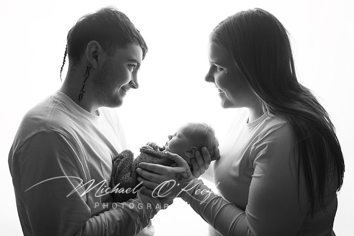 Black and white newborn photo of parents lovingly cradling their baby, captured by Michael O'Riley Photography.