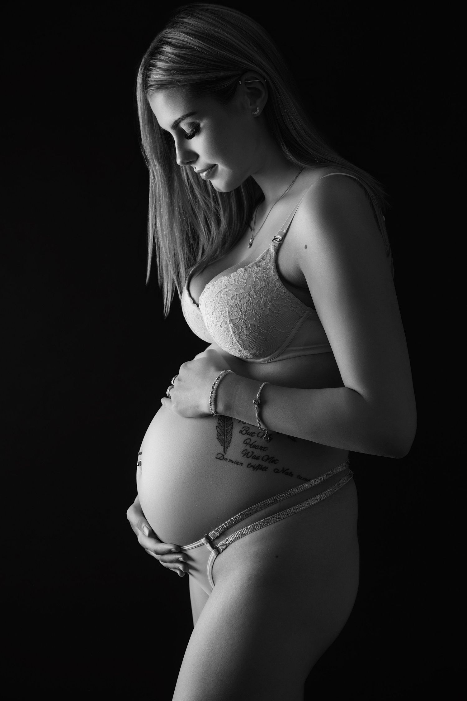 Black and white artistic maternity photo showing an expectant mother in lace lingerie cradling her pregnant belly.