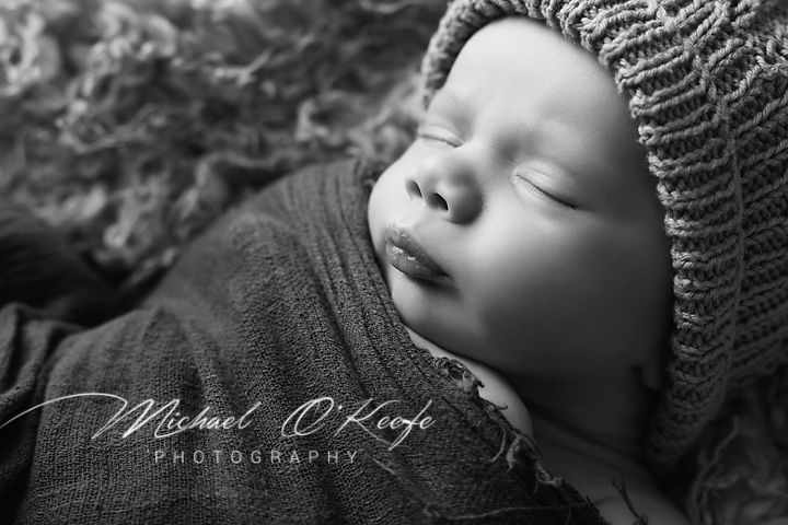 A peaceful sleeping newborn baby wrapped in soft knit fabric, captured in black and white photography.