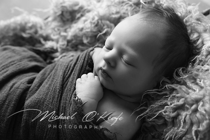 Black and white newborn photography of a sleeping baby wrapped in a soft blanket by Michael O'Keefe Photography.