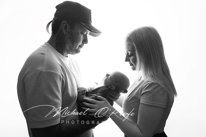 Black and white photo of new parents lovingly gazing at their newborn baby, studio portrait by Michael O'Keefe Photography.