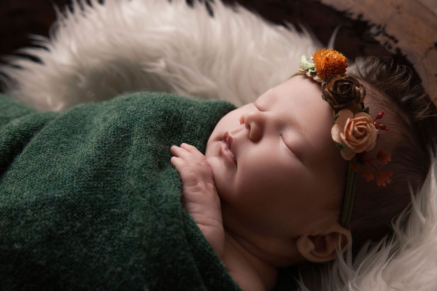 Baby lying on dark green blanket with small orange flowers in hair while sleeping peacefully.