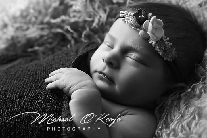 Black and white newborn photography with delicate floral headband against soft textured backdrop.