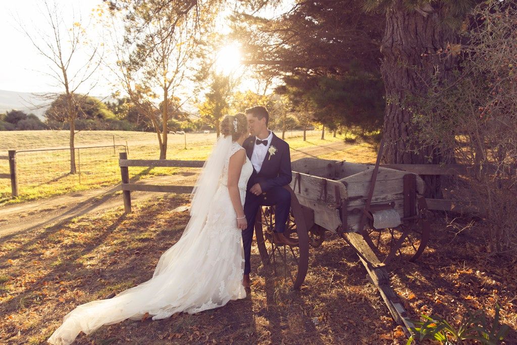 Wedding couple embracing near wooden fence during golden sunset in countryside.
