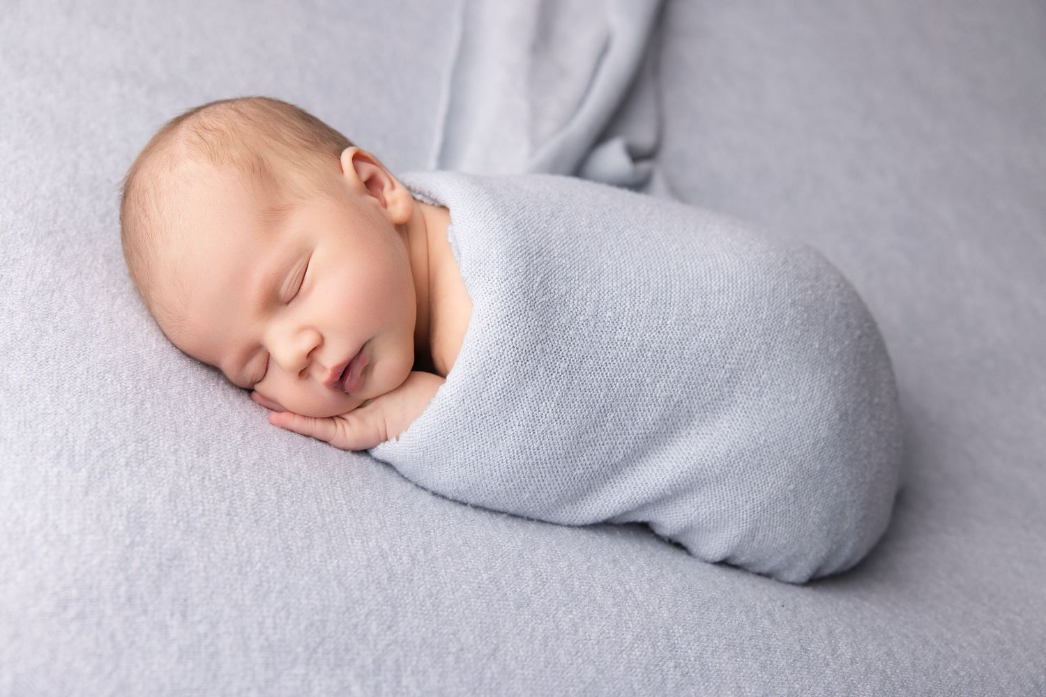 Peaceful newborn swaddled in soft gray wrap on light background.