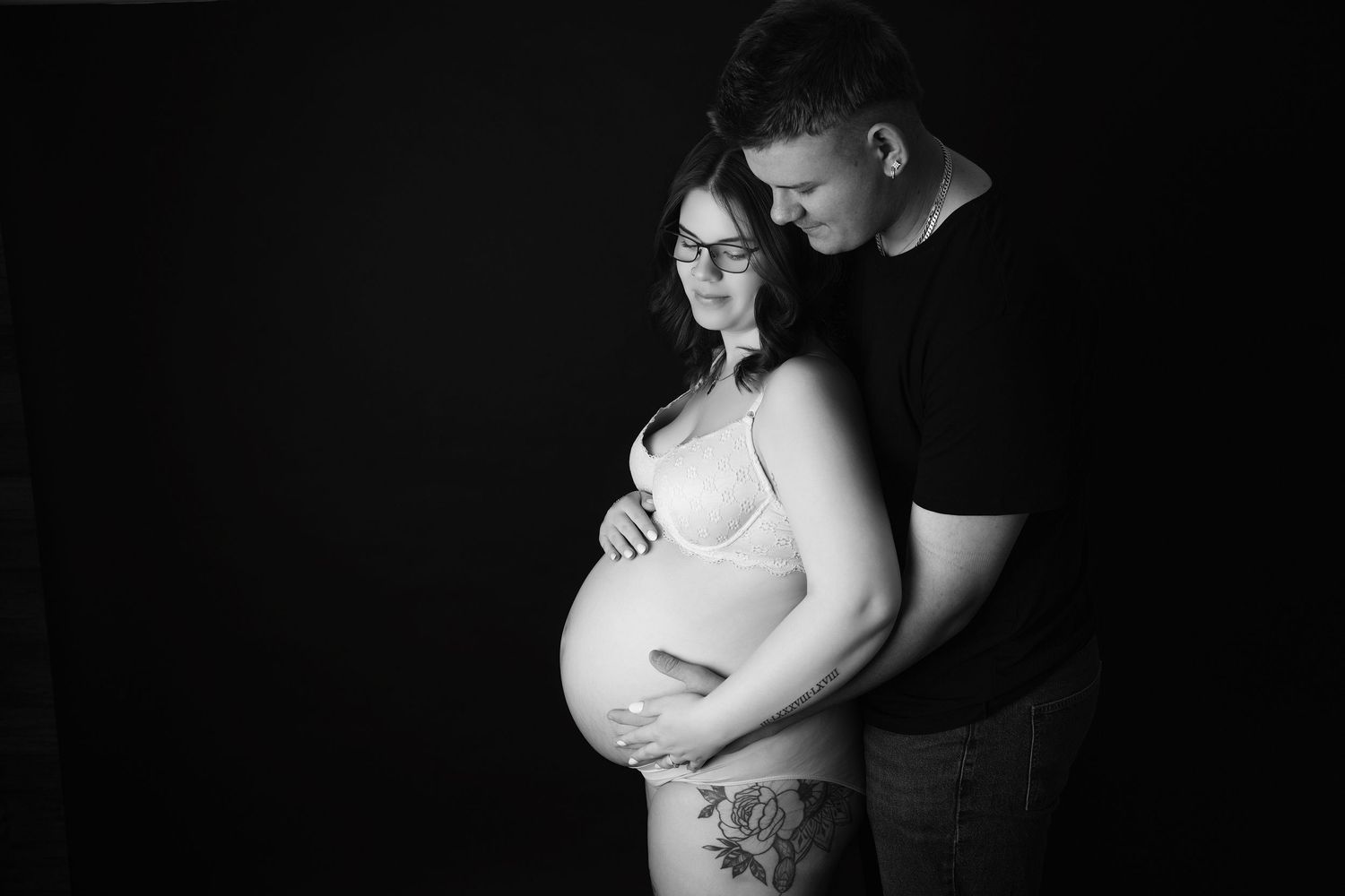 Artistic maternity photos captured against black background with dramatic lighting and intimate poses.