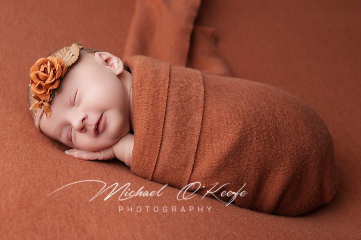 Peaceful newborn baby sleeping while wrapped in brown swaddle with floral accent.