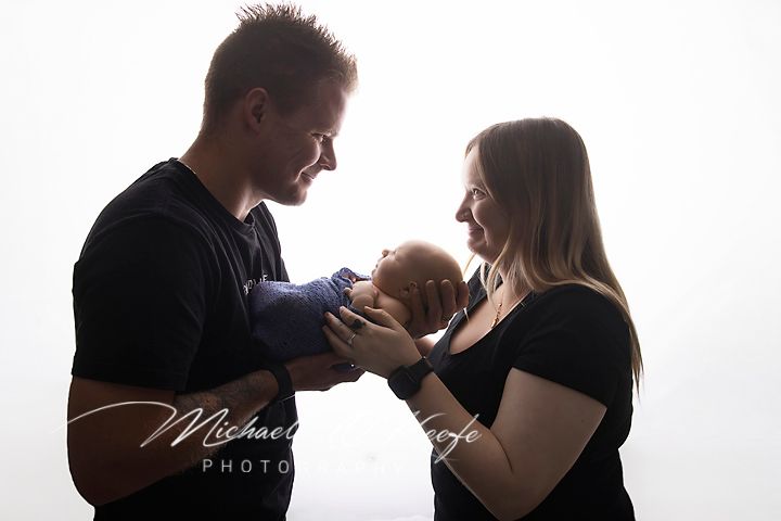 New parents lovingly hold their newborn baby together in a bright studio portrait by Michael Hof Photography.
