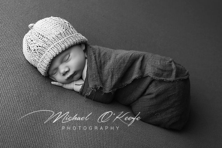 A series of black and white newborn photography images showing a sleeping baby in various poses with knit accessories.