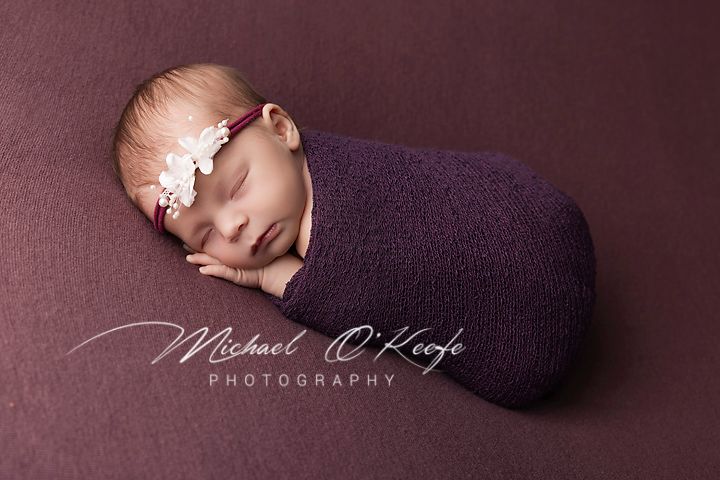 Newborn baby sleeping peacefully on purple blanket in professional studio photography setting.