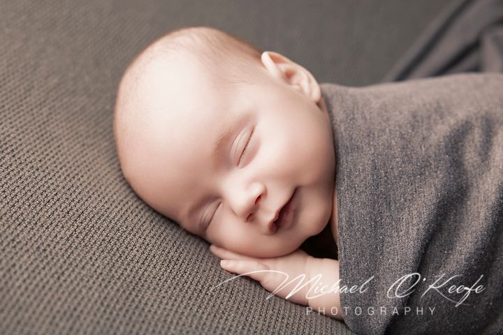 A sleeping baby peacefully rests on soft gray fabric in a professional studio portrait setting.