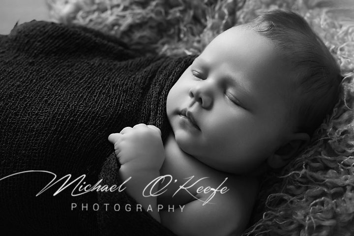 Black and white newborn portrait of a sleeping baby wrapped in a knit blanket by Michael O'Keefe Photography.
