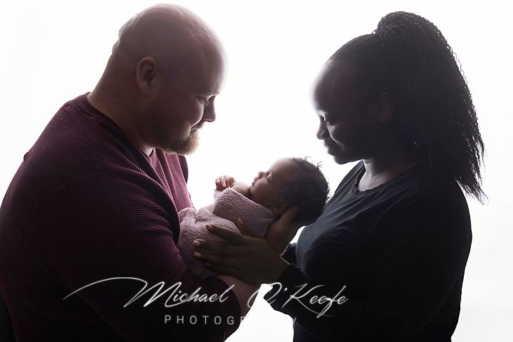 New parents tenderly holding their newborn baby in a softly lit studio portrait by Michael Keofe Photography.