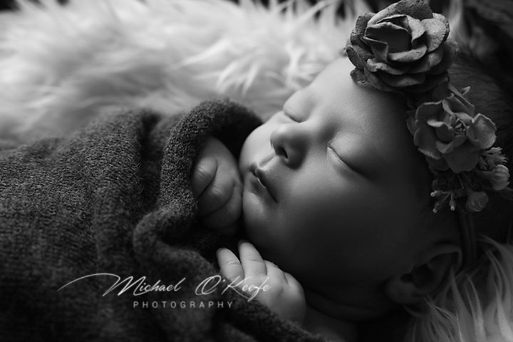 Peaceful newborn sleeping on soft white fur with dark floral accents in black and white portrait.