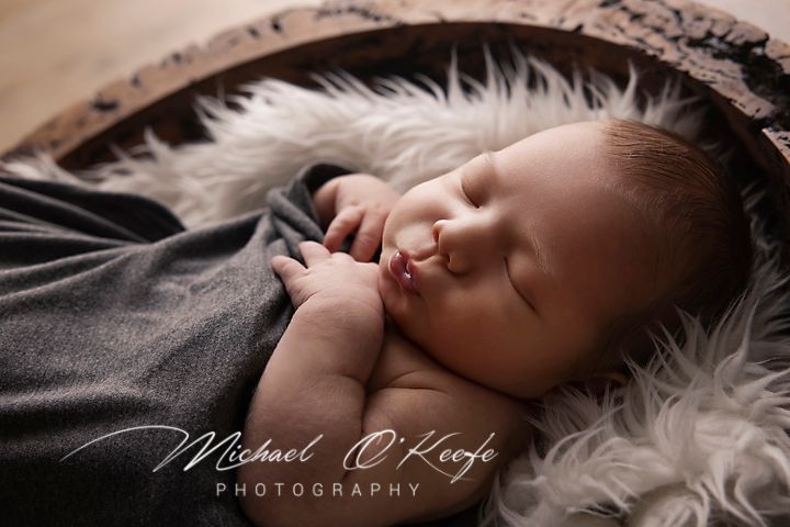Sleeping newborn on white fur with dark fabric in artistic portrait.