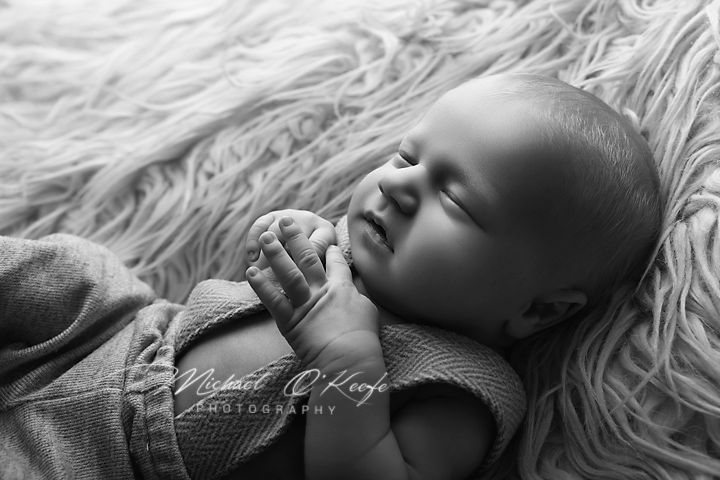 Black and white newborn photography of a sleeping baby with hands clasped, resting on a soft fluffy blanket.
