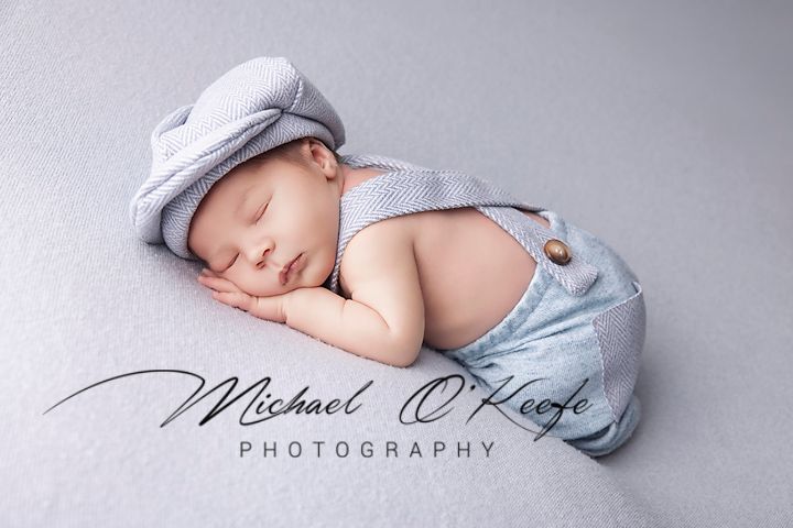 A sleeping newborn baby wrapped in soft gray fabric lies peacefully against a light gray backdrop.