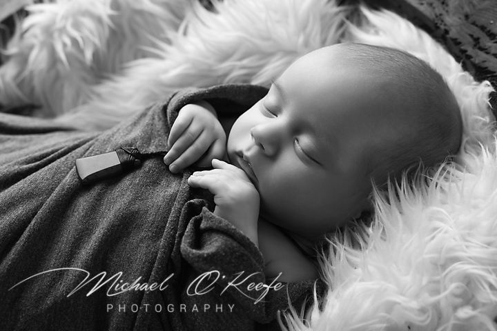 Black and white newborn photography portrait showing sleeping baby on soft white fur blanket.