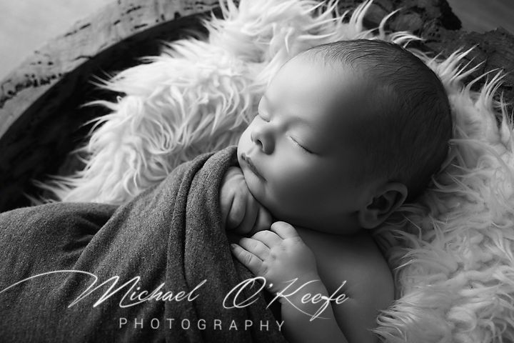 Black and white newborn portrait of a sleeping baby wrapped in a soft blanket by Michael O'Keefe Photography.