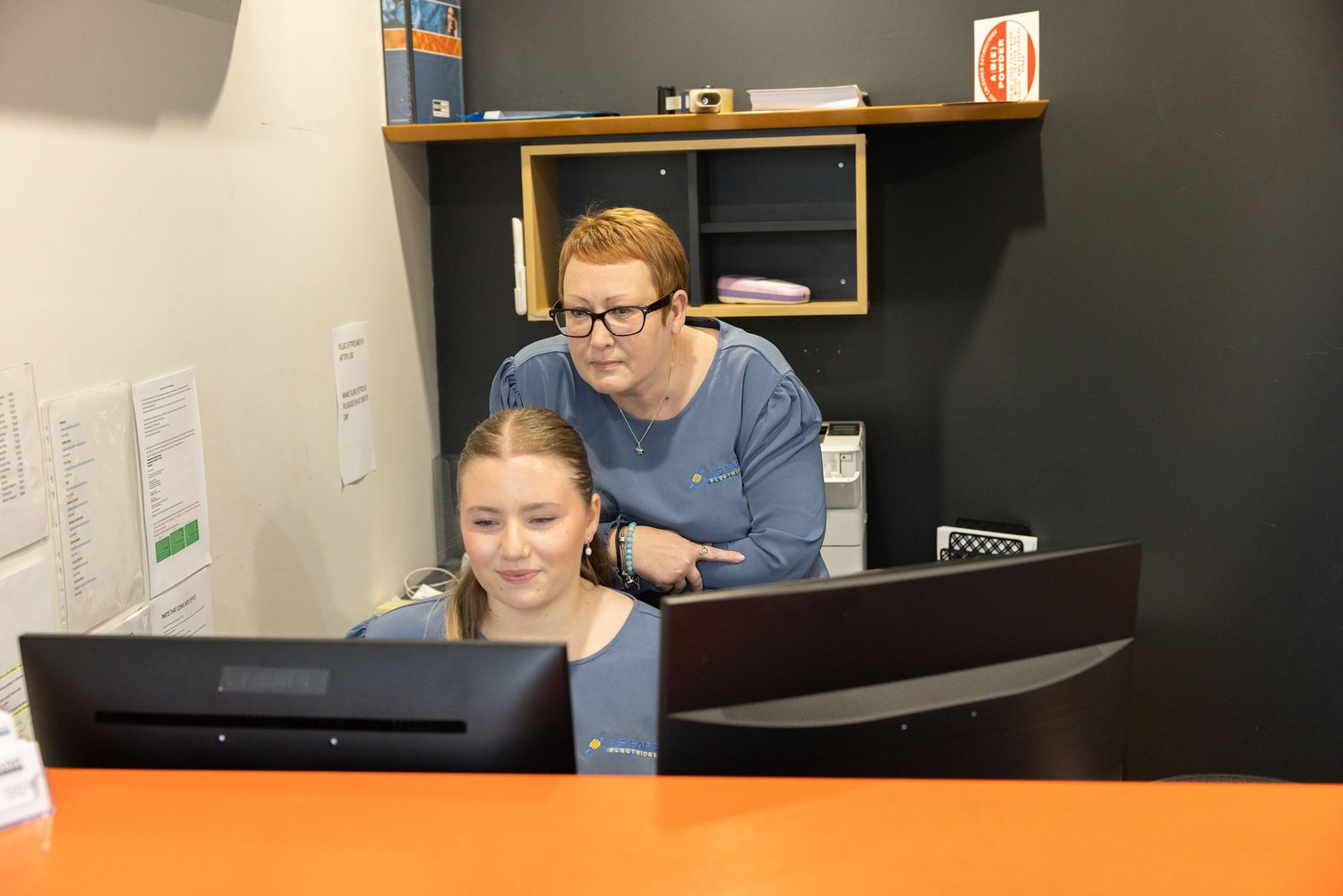 Two people collaborate while looking at a computer monitor in an office setting.