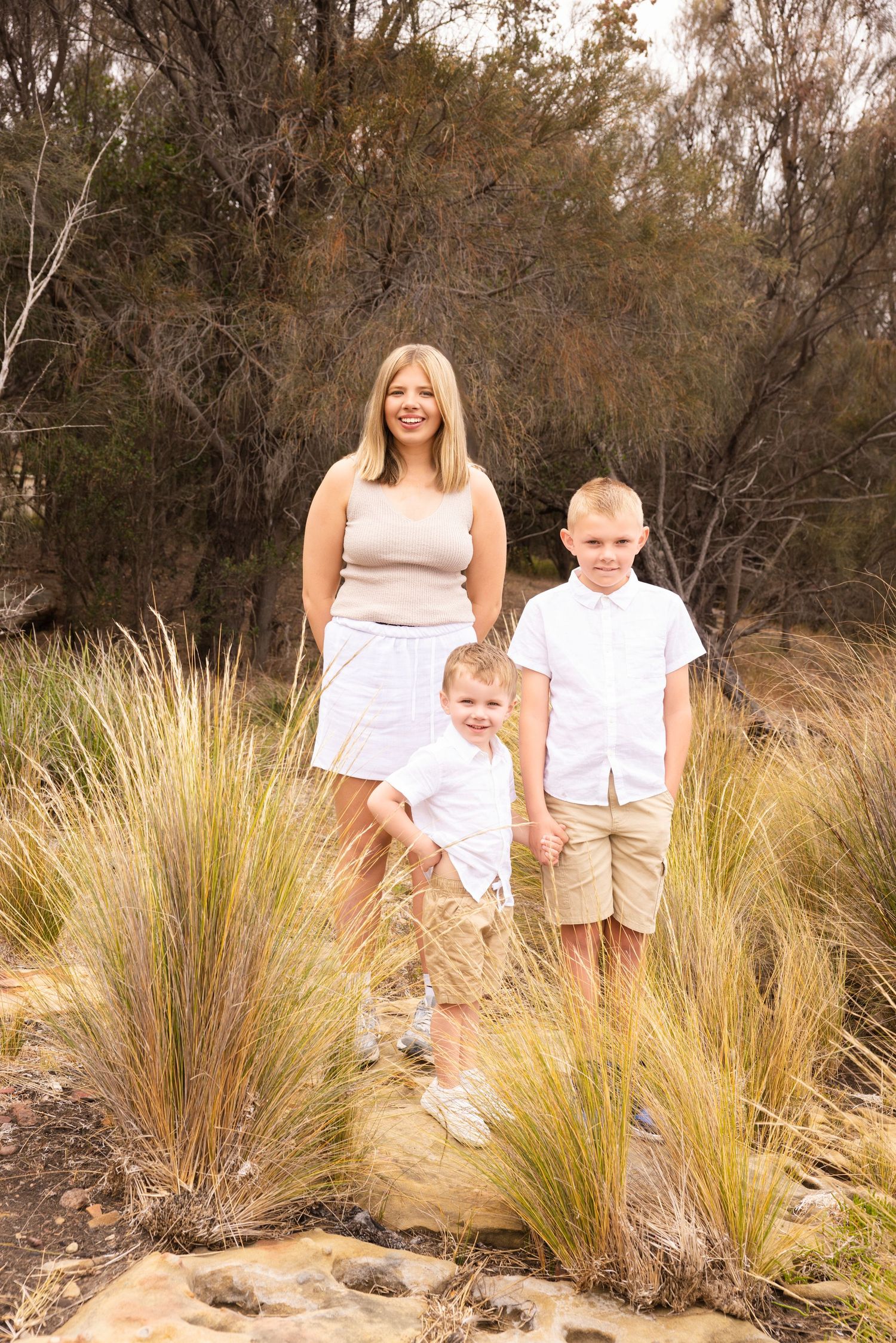 Family in white summer outfits poses together among tall grass in natural setting.