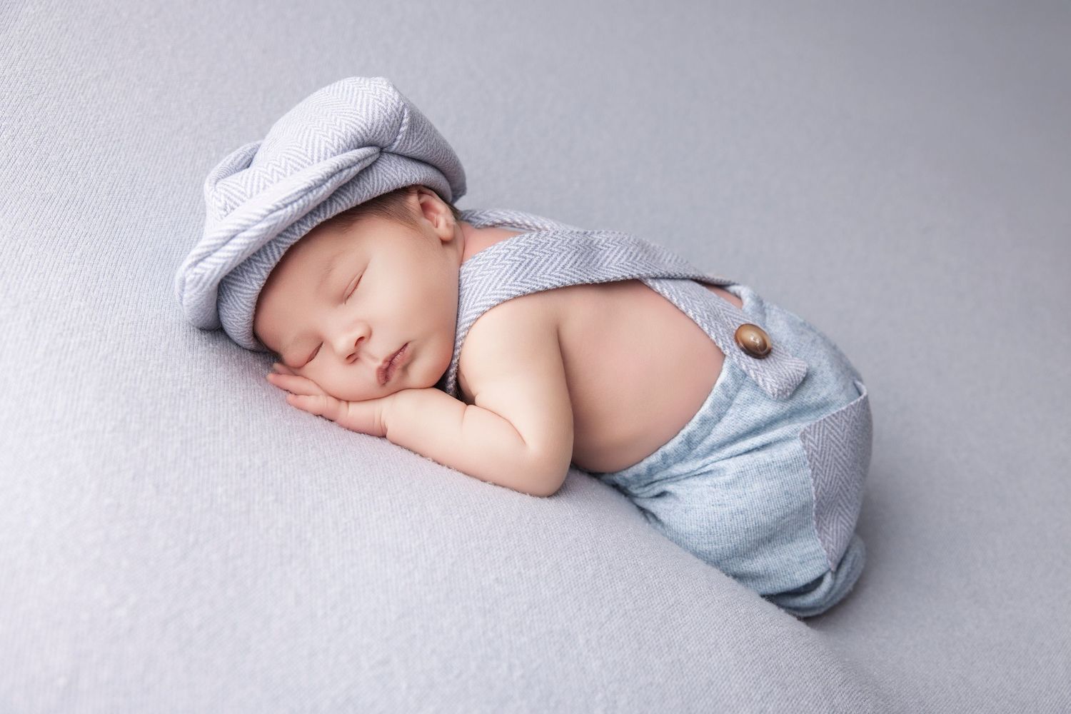 A sleeping newborn baby wearing a light blue wrap lies peacefully on a soft grey backdrop during a professional photo session.
