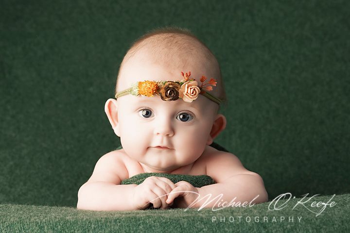 A baby in a white outfit sits against a dark green backdrop in a series of similar poses.