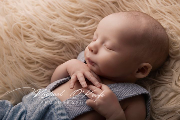 Peaceful sleeping newborn baby wrapped in blue fabric on a soft beige flokati fur rug, newborn photography.