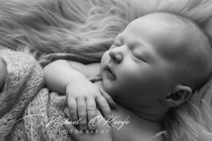 A peaceful sleeping newborn baby lies on soft fur in black and white photography.