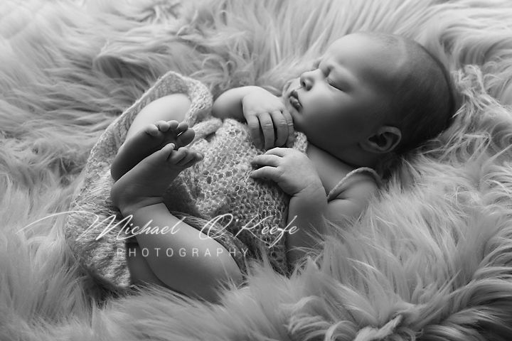 A newborn baby sleeps peacefully on soft white fur during a professional photography session.