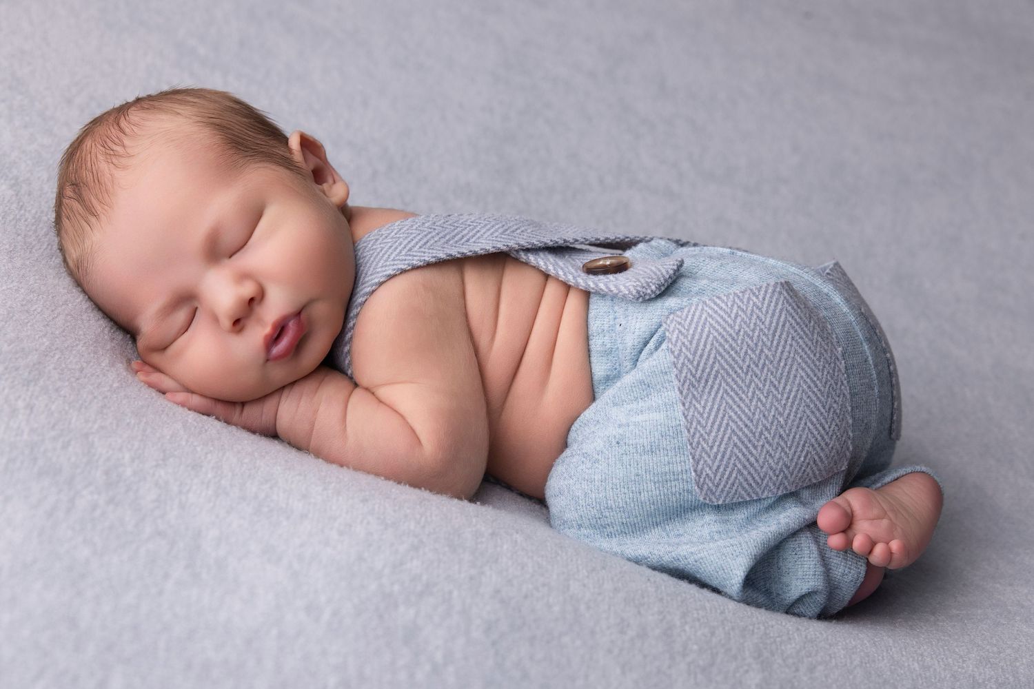Peaceful sleeping newborn wearing light blue shorts on grey backdrop.