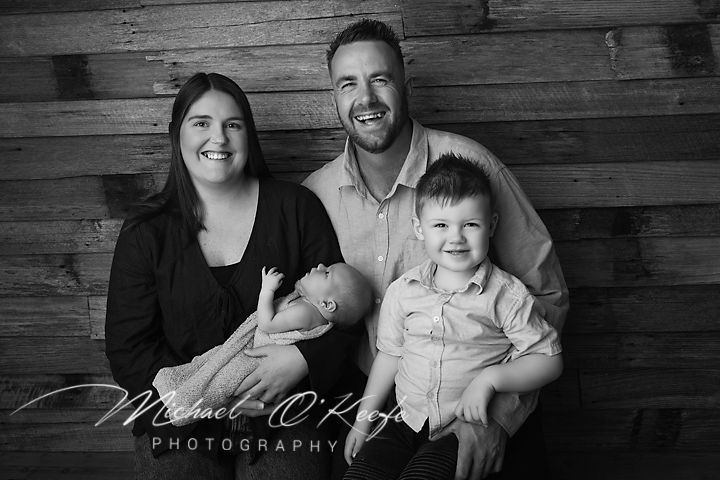 Black and white family portrait with parents, toddler son, and newborn baby by Michael O'Kay Photography.