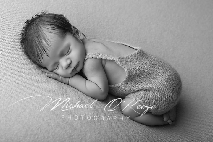 Black and white newborn photo of sleeping baby in knit romper, curled up peacefully by Michael O'Keefe Photography.