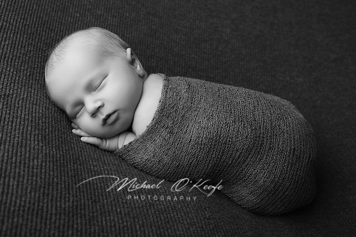 Black and white newborn photography of a sleeping baby swaddled in a soft wrap by Michael O'Keefe Photography.