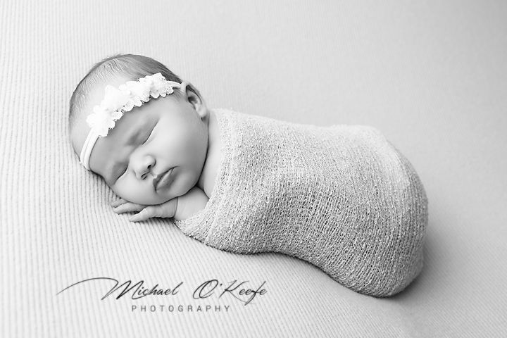 A series of four black and white photographs showing a newborn baby wrapped in soft blankets.