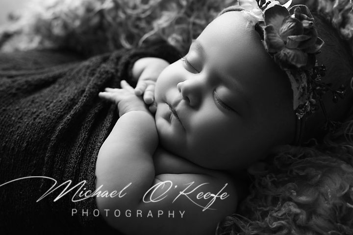 Black and white newborn portrait of a sleeping baby with floral headband by Michael O'Keefe Photography.