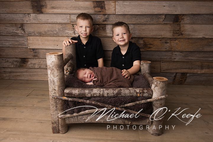 Two children pose together on a rustic wooden bench against a weathered plank wall background.