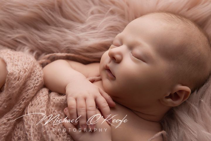 Sleeping newborn baby lying on soft pink fabric during professional photography session.