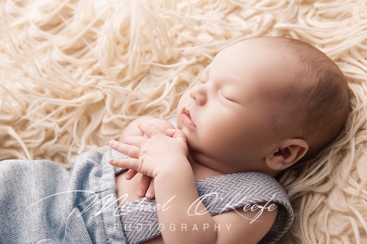 Newborn baby sleeping peacefully on soft cream-colored textured blanket in natural light.