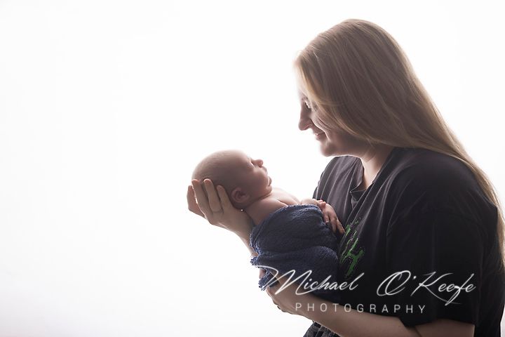 A mother tenderly holds her newborn baby in a softly lit studio portrait by Michael O'Keefe Photography.