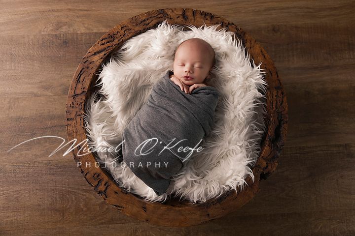 Newborn baby sleeping peacefully on soft white fur against rustic wooden backdrop in professional photography setup.