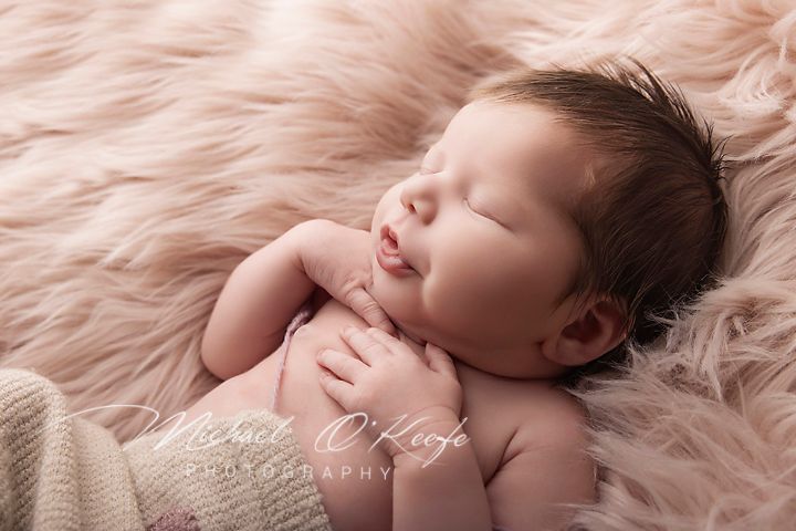 Peaceful newborn baby sleeping on soft pink fur blanket, smiling sweetly with tiny hands clasped together.