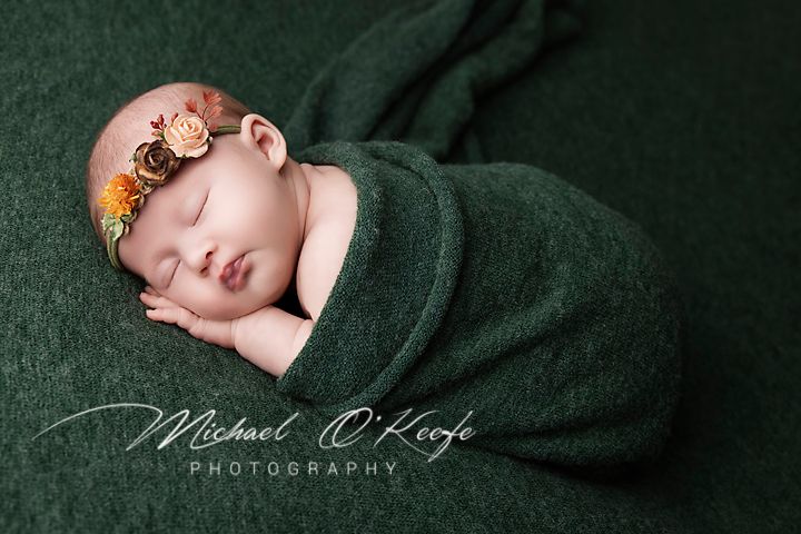 Newborn sleeping peacefully in green wrap with delicate floral crown.