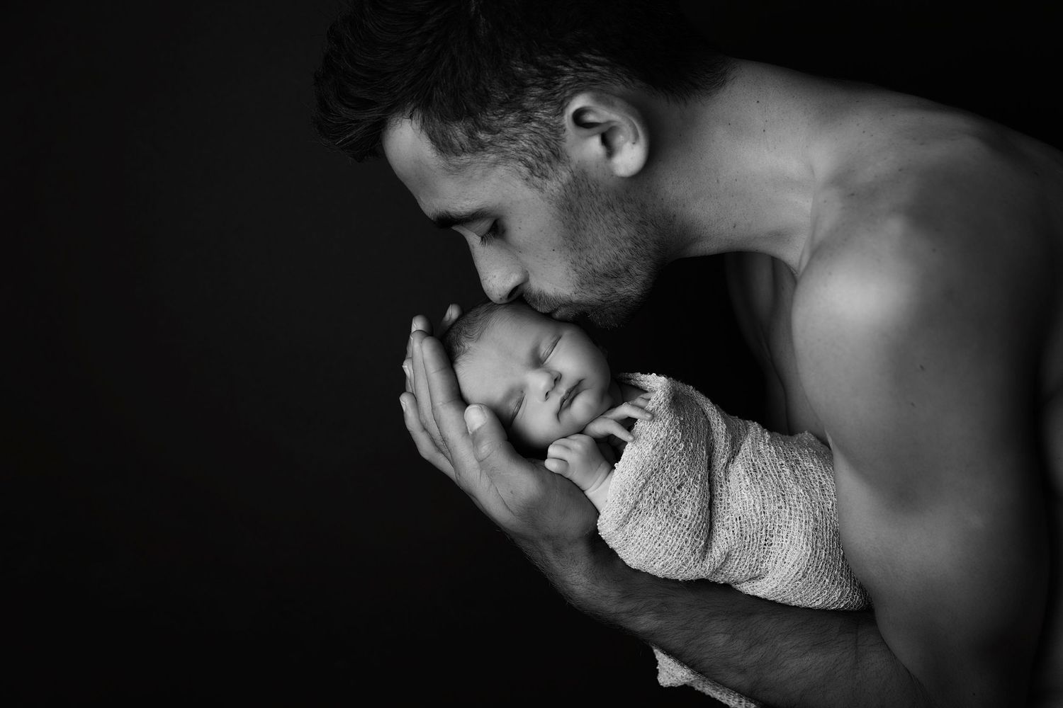 Intimate black and white portrait showing tender moment between parent and newborn.