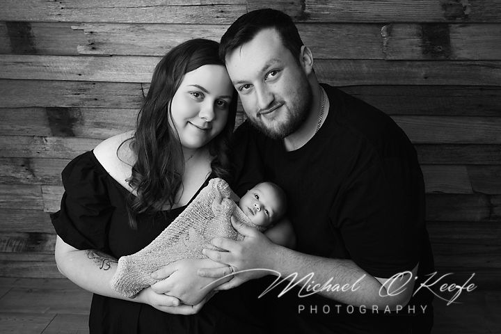 A couple poses intimately against a rustic wooden wall backdrop in black and white photography.