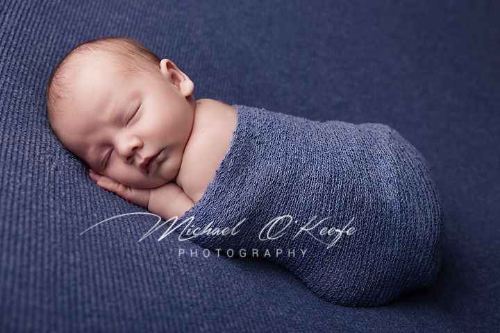 A sleeping newborn baby swaddled in navy blue fabric during a professional photography session.