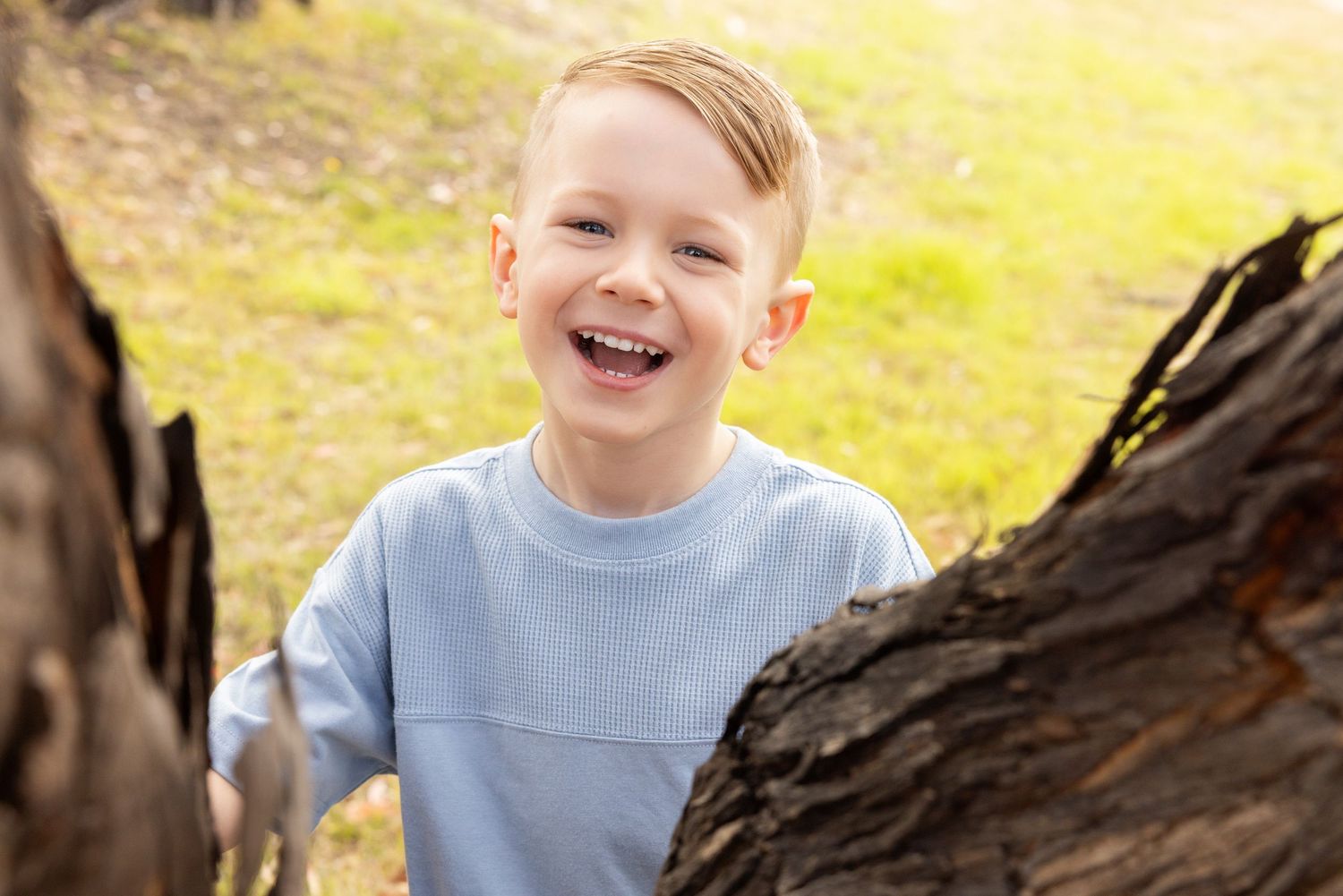 Joyful candid moment of child laughing while playing near tree trunk outdoors.