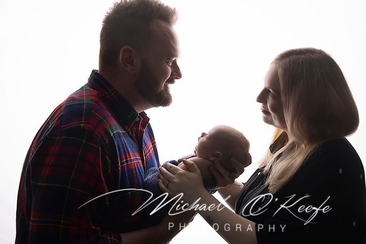 New parents smiling at their newborn baby in a bright studio portrait by Michael O'Keefe Photography.