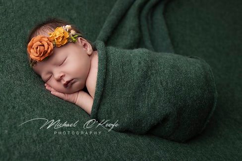 Peaceful sleeping newborn wrapped in deep green fabric with artistic lighting.